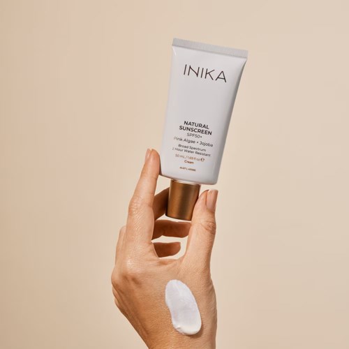 En hånd holder en tube med INIKA naturlig solkrem med en klatt krem på huden.