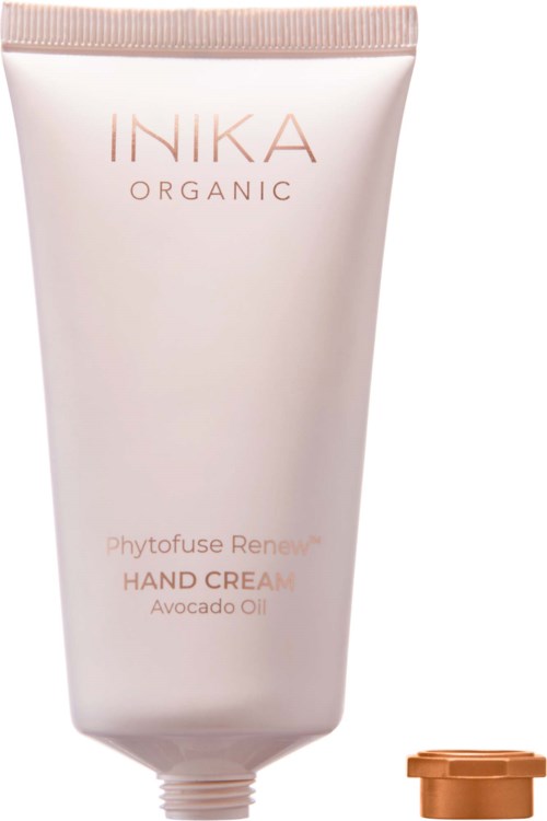 A white tube of INIKA Organic Hand Cream with avocado oil, with a small copper-colored lid placed nearby.