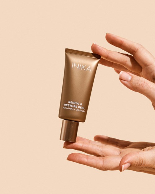 A hand holds a gold-colored tube of skincare cream with text, against a light beige background.