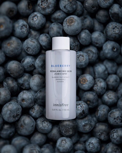 Een huidverzorgingsfles omgeven door veel verse bosbessen, die blauweberry-extract ingrediënten benadrukken.