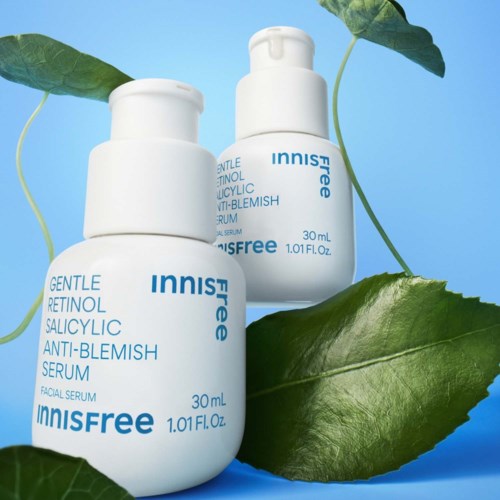 Två vita flaskor med Innisfree hudvårdsserum placerade bland gröna blad på en blå bakgrund.