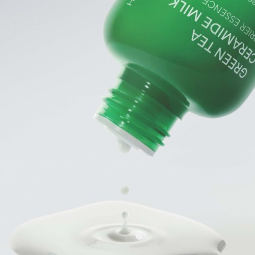 Grön behandlingflaska med vitt krämmönster som rinner ut och bildar en liten splash.
