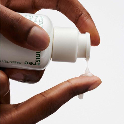 En hand trycker ut lotion eller serum ur en vit flaska på ett finger.