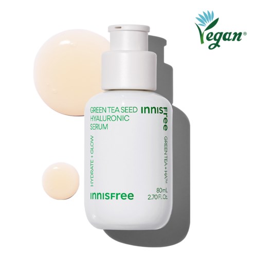 Een witte huidverzorgingsfles met label 'Innisfree Green Tea Seed Hyaluronic Serum' en twee crème-achtige druppels ernaast.
