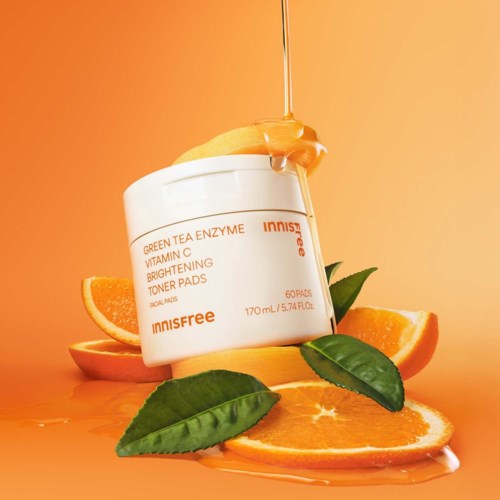 En burk med Innisfree Vitamin C Brightening Toner Pads omgiven av apelsinskivor och gröna blad på en varm orange bakgrund.