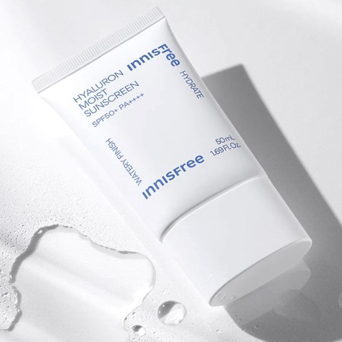Een witte tube zonnebrandcrème met blauwe tekst ligt op een witte oppervlakte. In de buurt is zonnebrand gespeten.