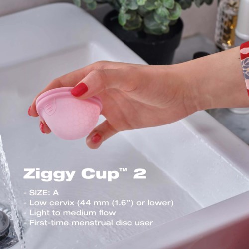 Eine Hand hält eine rosa Menstruationstasse über einem Waschbecken, mit Produktinformationen darunter, einschließlich Größe und Funktionen.