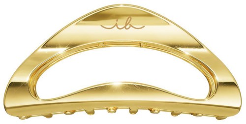 A shiny, golden hair clip with a curved design and small teeth for holding hair. There is a logo or design on it.