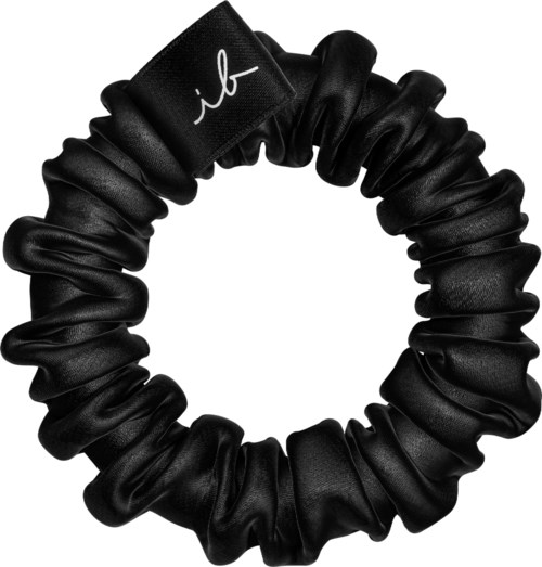 A black scrunchie with a small white logo or initials on it. It is made of shiny fabric and looks soft.
