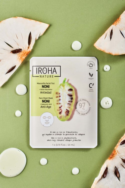 Gezichtsmasker-verpakking met kiwi-afbeelding, omgeven door kokosnootschijven en verspreide witte tabletten op een groene achtergrond.
