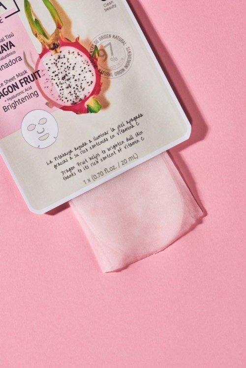 Verpakking van een huidverzorgingsproduct met afbeelding van drakenfruit, roze achtergrond en roze doek eronder.