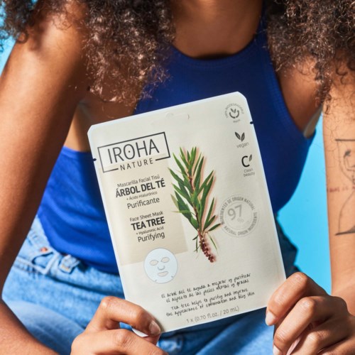 Een vrouw houdt een gezichtsmasker met Tea Tree illustratie en huidverzorgingsinformatie.