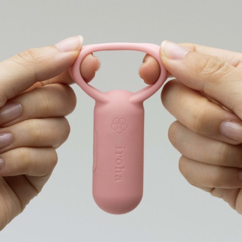 Eine Person hält ein kleines rosa Silikonwerkzeug mit zwei Fingeröffnungen und einer Blumenzeichnung, beschriftet "ioma."
