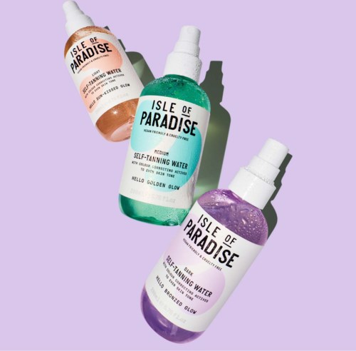 Three bottles of Isle of Paradise self-tanning water in different colors: peach, green, and purple. They have spray nozzles and labels.