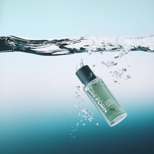 Een groene fles met 'Hydro Boost' zinkt in water, waardoor er bellen en spetters ontstaan.