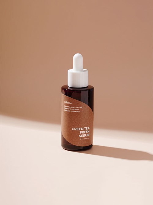 Een kleine bruine fles met pipet, label 'Green Tea Fresh Serum,' staat op een beige achtergrond.