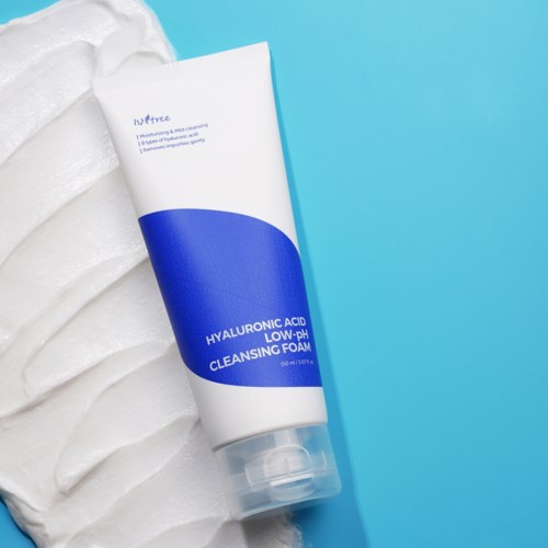 Een tube met hyaluronzuur reinigingsschuim op een blauwe achtergrond met witte golven ernaast.