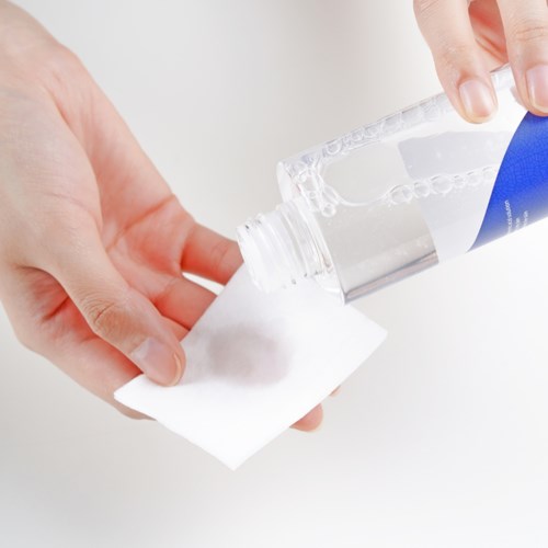 Iemand schenkt handdesinfecterend uit een fles op een wit doek. De achtergrond is simpel en licht.