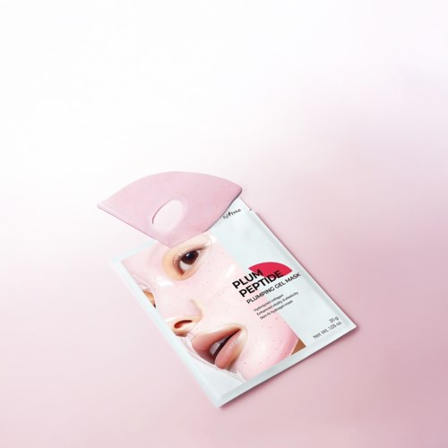 Een gezichtsmasker-verpakking met gezicht afbeelding en roze verpakking, op lichtroze achtergrond.