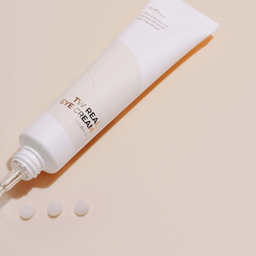 A tube of eye cream, three small white pills beside it, on a light background.