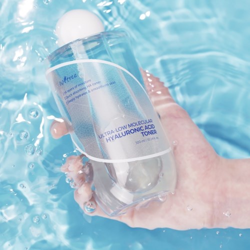 Een hand houdt een doorzichtige fles met hydraterende toner in een helderblauw zwembad.