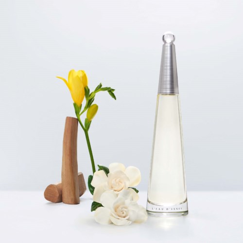 Een kleine houten sculptuur met een gele bloem, witte bloemen en een lang glazen parfumflesje.