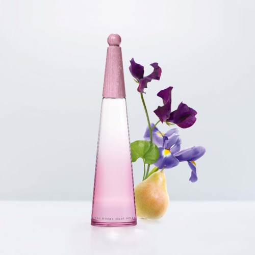 Een roze parfumfles, gele peer en paarse bloemen samengebracht op een lichte achtergrond.
