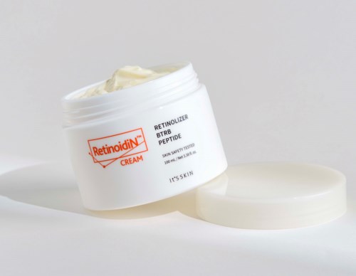Ein weißer Behälter mit Retinol-Creme und einem Deckel daneben, auf einer weißen Oberfläche.
