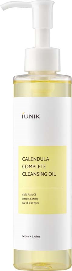 Een lange witte fles met pomp, labeled 'Calendula Complete Cleansing Oil,' bevat gele vloeistof voor huidreiniging.