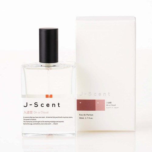 En genomskinlig parfymflaska med svart lock och en vit box bredvid, båda märkta J-Scent, på vit bakgrund.