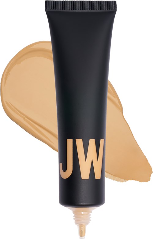 En svart tub med gyllene bokstäver 'JW' framför en beige foundation.