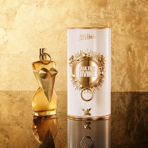Een gouden parfumfles met gedetailleerde dop en een lange witte doos met gouden ontwerp en tekst.