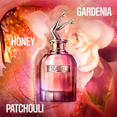 Een parfumfles met een gouden deksel in de vorm van benen, gemerkt Scandal, omgeven door bloemen en roze bladeren.