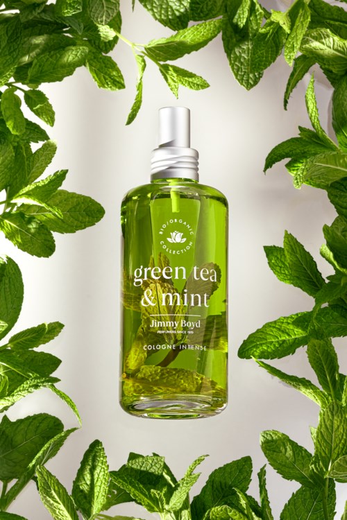 Een colognefles met groene thee en munt, omgeven door verse muntblaadjes.