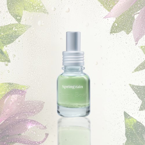 A small perfume bottle labeled Spring Rain with a silver cap, surrounded by water droplets and pastel leaves.