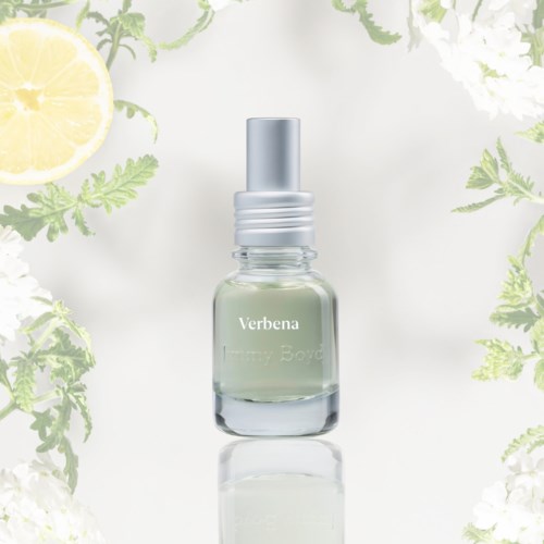 A perfume bottle surrounded by lemons, green leaves, and white flowers on a white background.