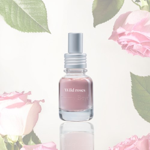 A perfume bottle labeled Wild roses surrounded by pink roses and green leaves.