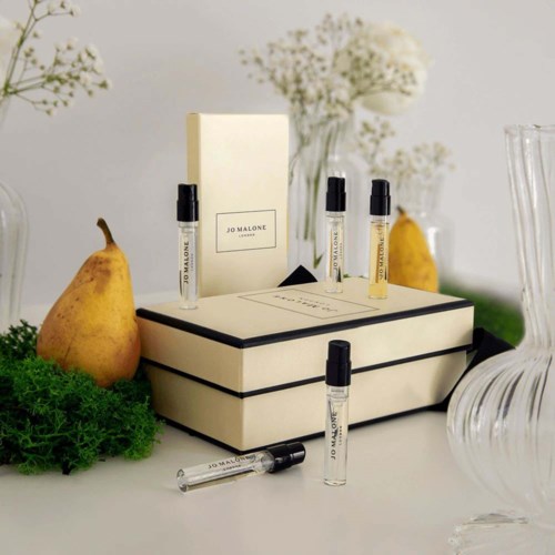 Jo Malone perfume samples, some in small spray bottles, arranged around a white box, with pears and flowers nearby.