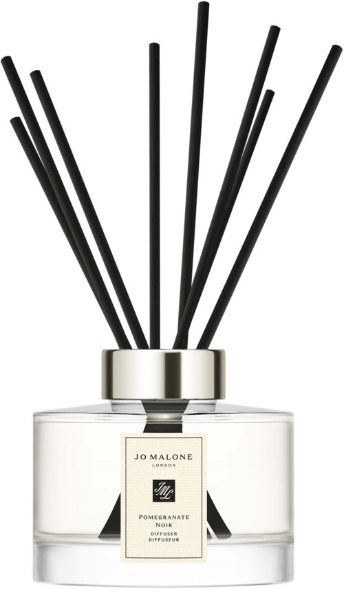 Valkoinen lasiastia mustilla tikkuilla sisällä, merkitty Jo Malone Pomegranate Noir -tuoksuksi, näyttää tyylikkäältä.