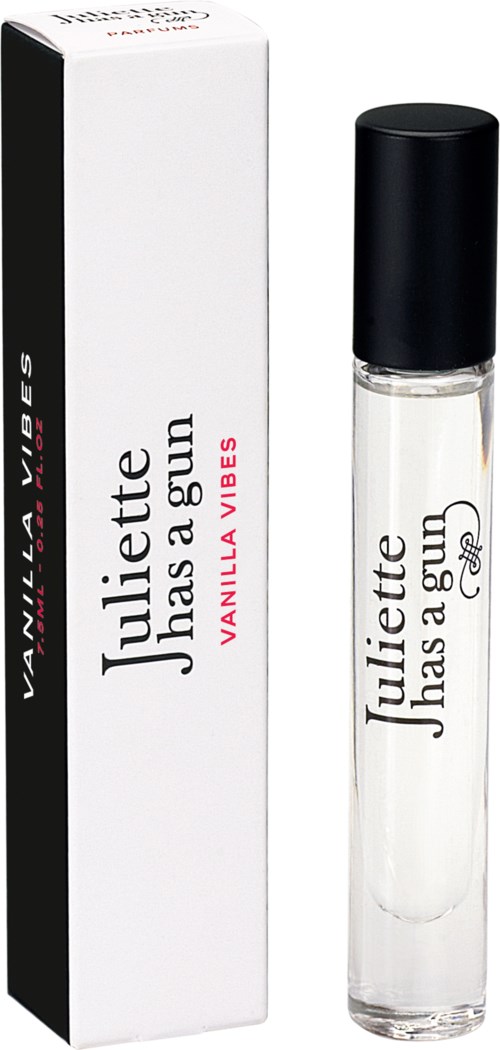 Eine kleine Parfümflasche mit Vanilduft neben einem weißen Karton mit schwarzem und rosa Text.