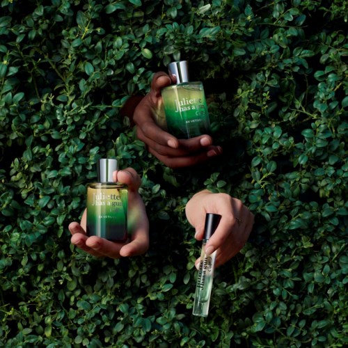 Three hands hold different perfume bottles against a green leafy background.