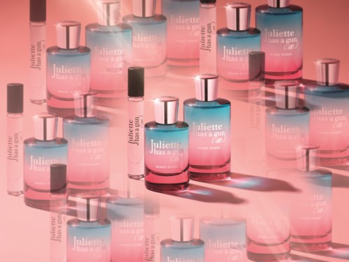 Meerdere parfumflesjes in roze en blauw, enkele verspreid op een reflecterend oppervlak met een wazige achtergrond.