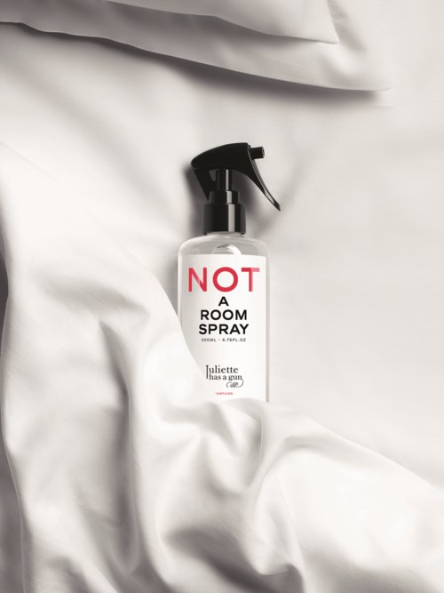 Een sprayfles met een label dat zegt "NOT A ROOM SPRAY" ligt op wit stof.