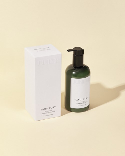 A green bottle of hand lotion with a pump and its white box box on a light background.
