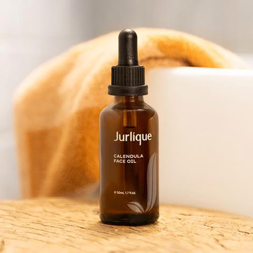 Een klein bruin flesje met Jurlique Calendula Face Oil met druppelaar, op een houten oppervlak.
