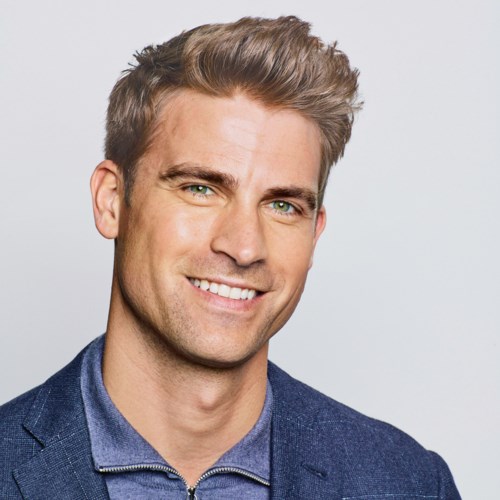 A smiling man with short, styled brown hair, light skin, dressed in a blue blazer and shirt.