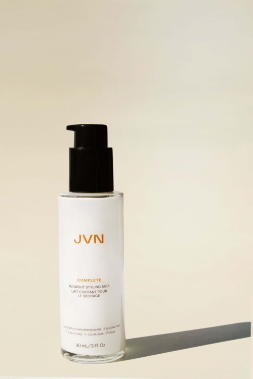 Kleine weiße Sprühflasche mit JVN-Label auf einer ebenen Fläche, wirft Schatten. Der Hintergrund ist einfach.
