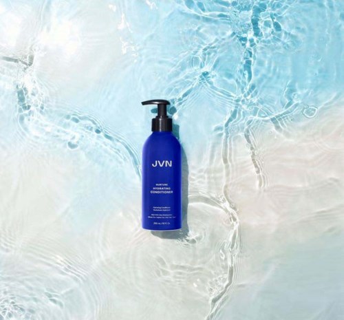 Eine blaue Flasche mit JVN liegt im klaren, flachen Wasser mit sanften Wellen.