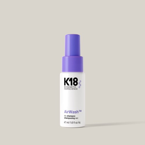 A small white bottle with a purple cap labeled K18 AirWash dry shampoo. It is standing upright.