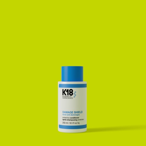 A bottle of K18 Damage Shield hair conditioner on a bright green background.